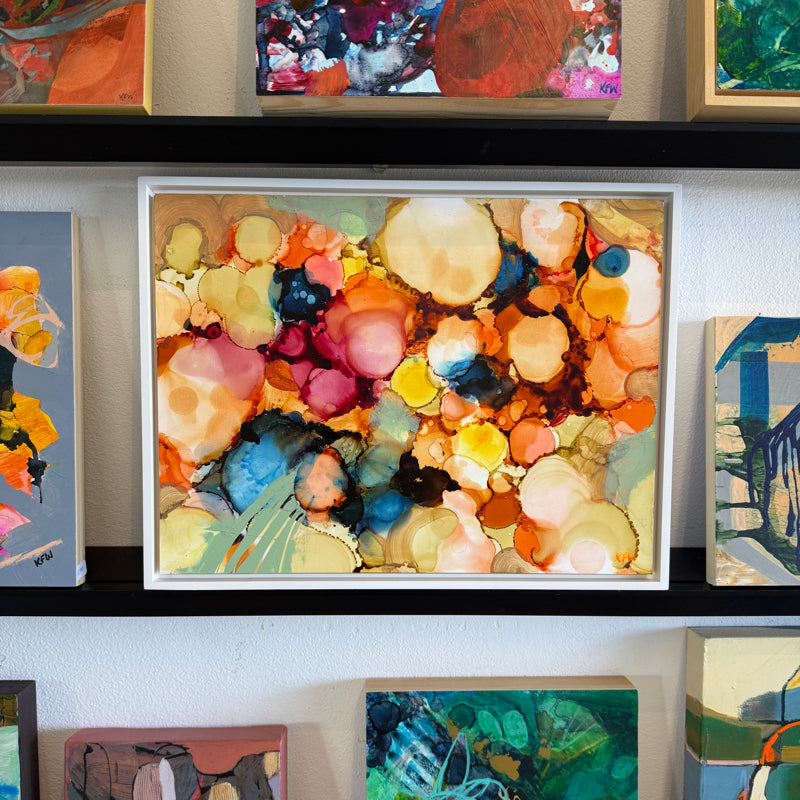 Framed abstract artwork with colorful circles on a wall with other artworks.