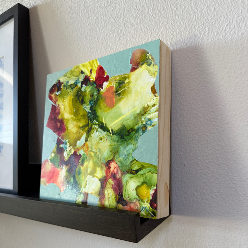 Colorful abstract painting on a wooden panel leaning against a white wall.