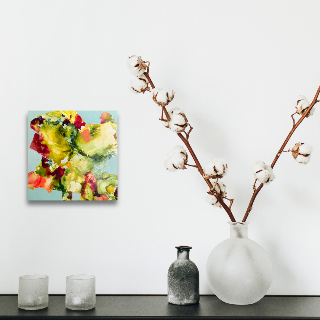 Decorative setup with a colorful abstract painting, vase with cotton branches, and small bottles on a shelf.