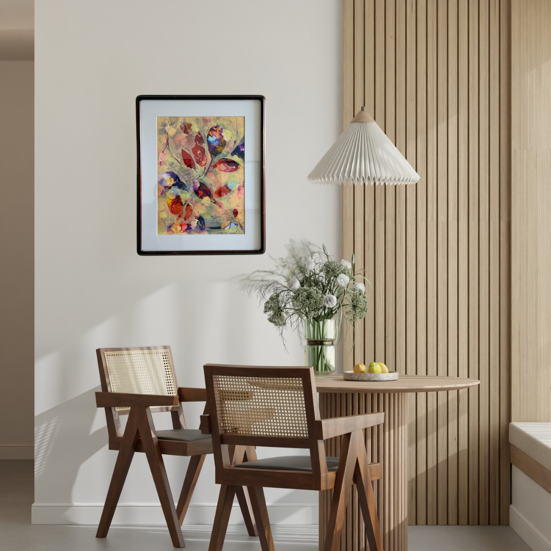 A framed abstract floral art print hangs on a beige wall in a modern dining room setting with wooden chairs, a slatted wood table, and a pleated white pendant lamp.