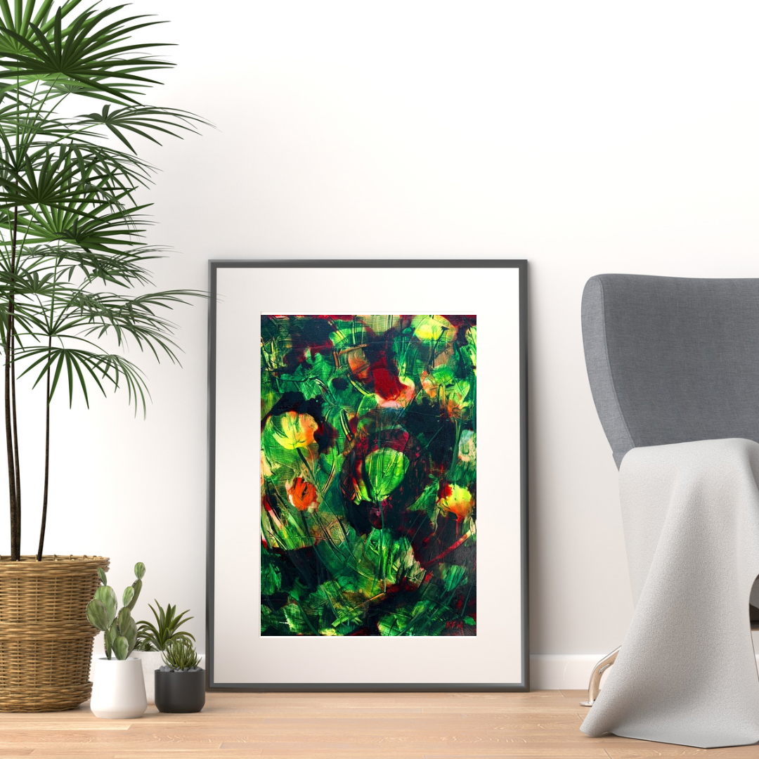 A framed abstract art print featuring vibrant green, red, and yellow brushstrokes, styled in a modern room setting next to a gray armchair and potted plants.