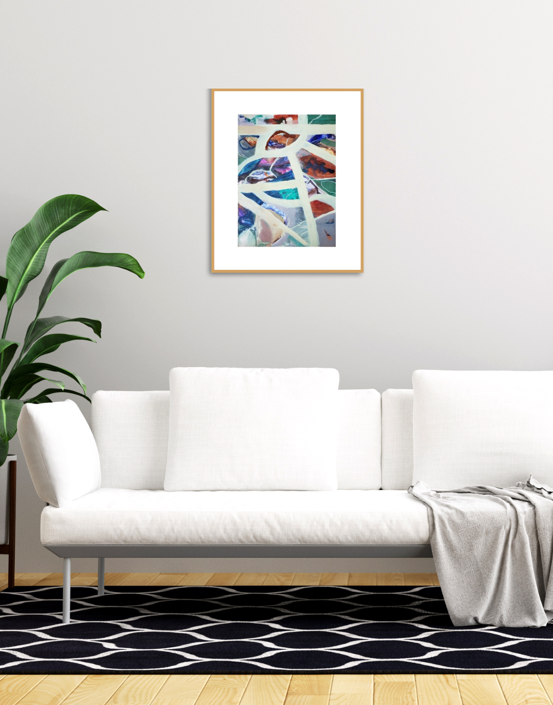 A framed abstract art print with colorful geometric patterns hangs on a light gray wall above a modern white sofa in a styled living room setting.