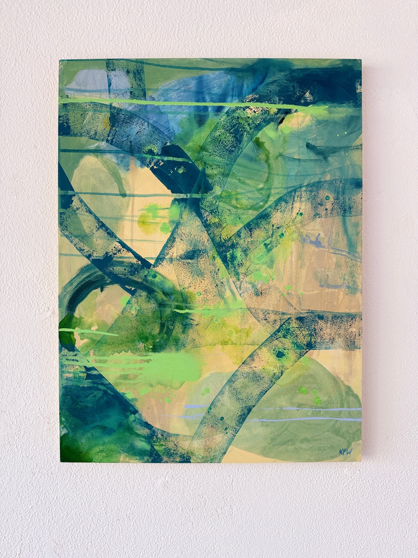 An abstract canvas painting featuring layered brushstrokes and splatters in shades of green, blue, beige, and black, displayed on a textured off-white wall.